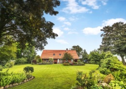 Red brick house in a beautiful garden in the summer with a green lawn under a blue sky