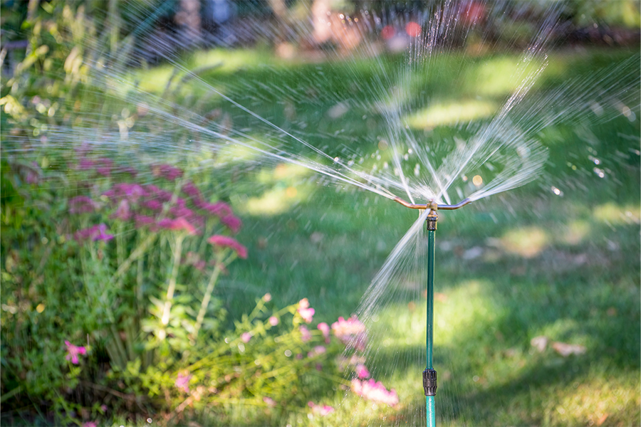 Water sprinklers running on a lawn with various flowers.
