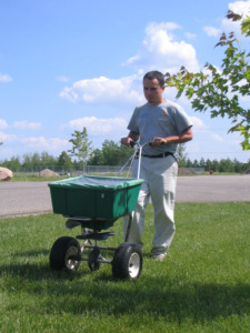 Soil amendments like gypsum or lime being applied to a lawn with a push cart by a Valley Green employee.