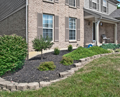 A mulch bed with ornamental plants surrounding a house.